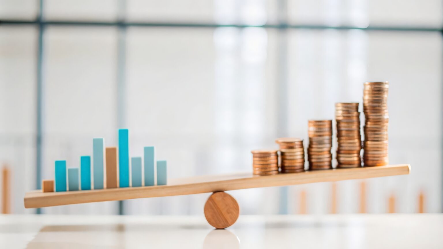 Simple graphic depicting a seesaw with coin piles balanced on one side, representing profit, and graphs on the other, depicting business data