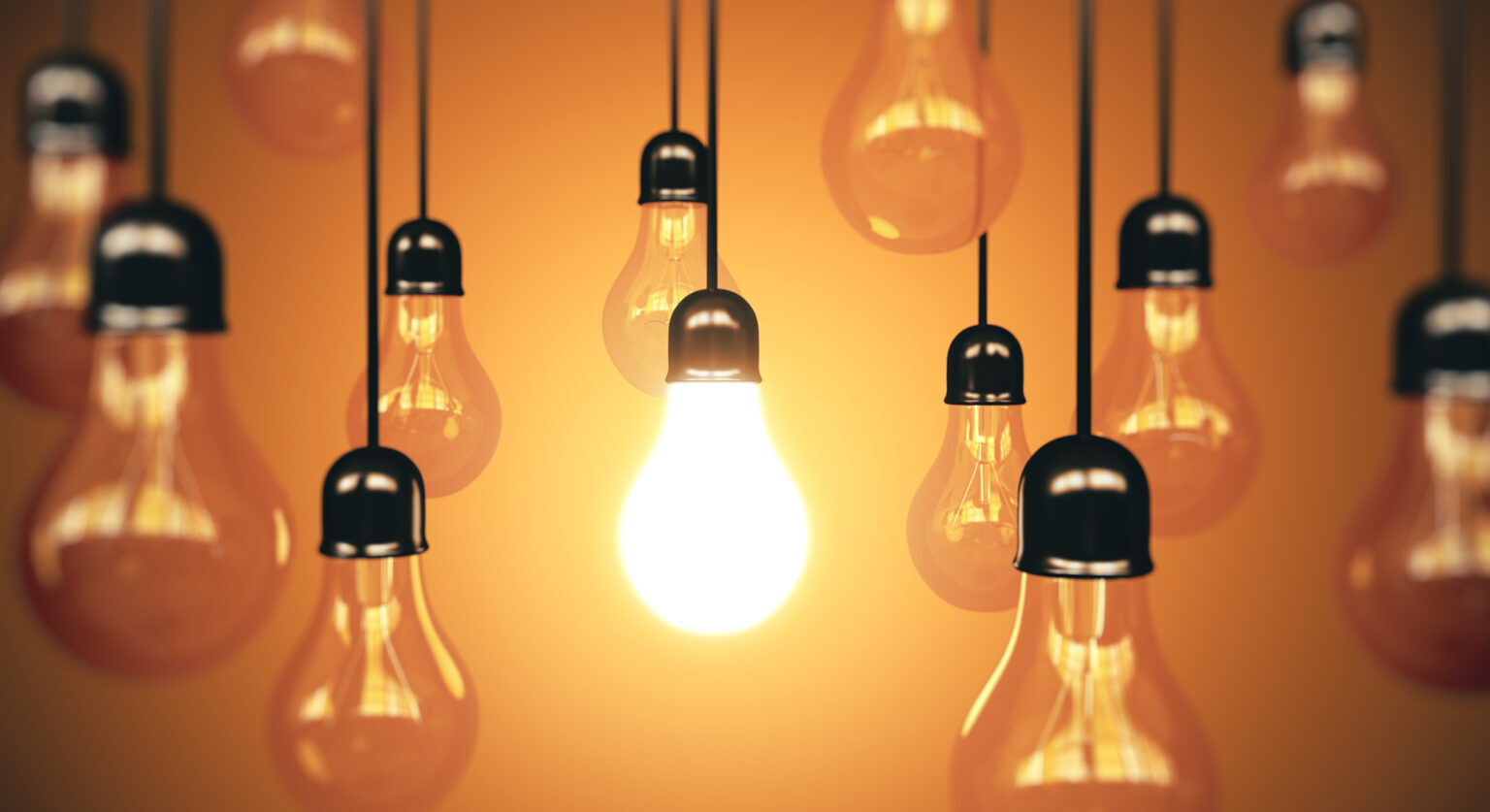 A bunch of lightbulbs hanging from the ceiling with one bulb lit