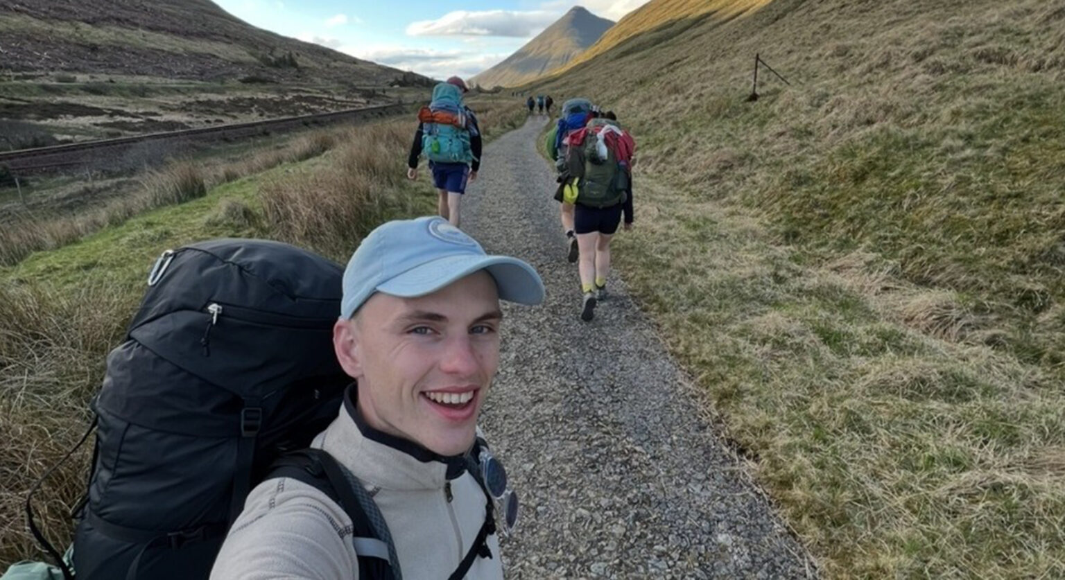 A man on a hike taking a selfie with a view of the mountains behind him