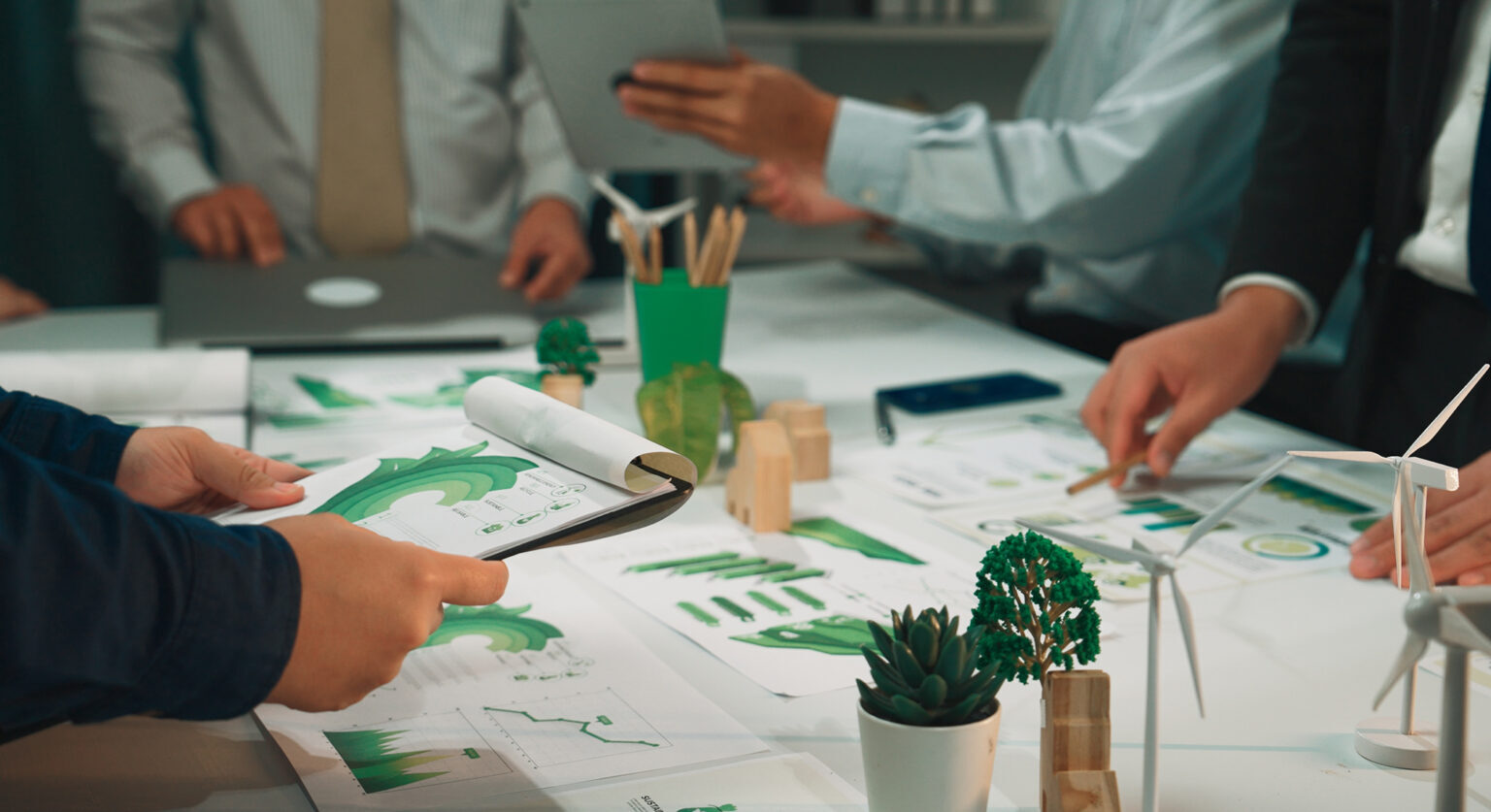Business people at a table with green charts and reports on it