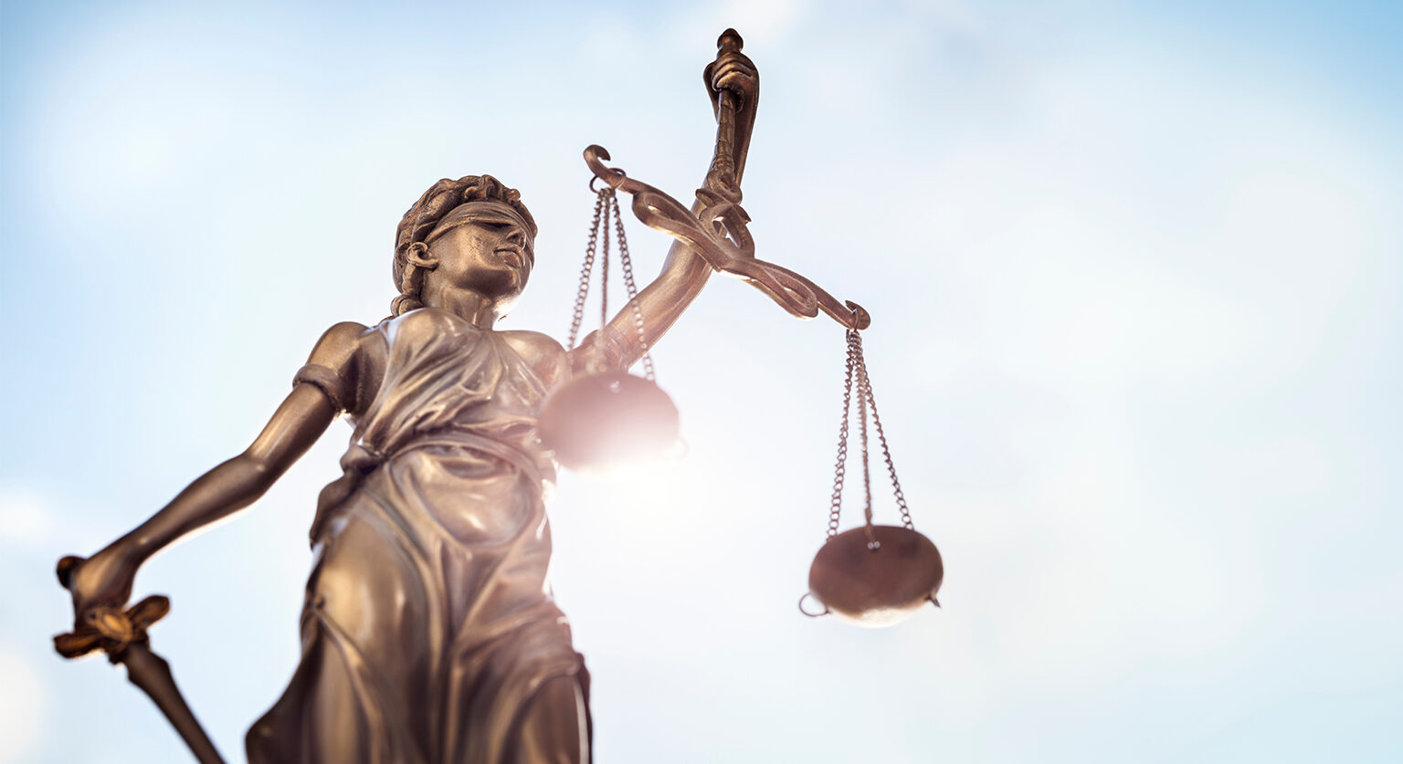 A statue of lady justice with the sun as a backdrop