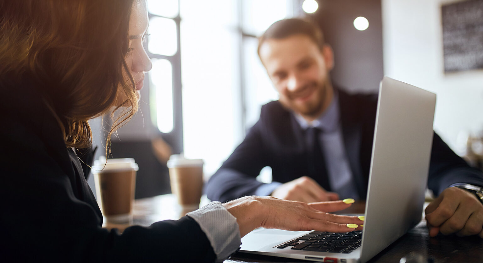 A man and a woman talking at a desk pointing at a laptop screen